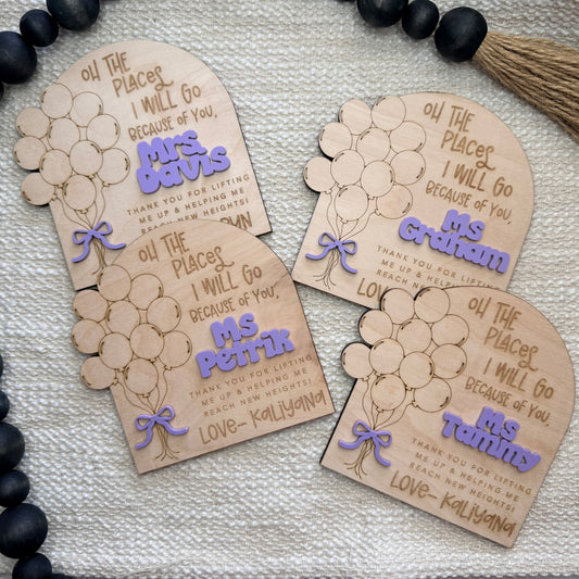 Personalized wooden name tags with balloon designs on a textured surface.